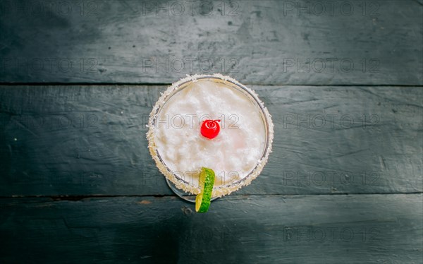 Top view of delicious frozen coconut cocktail with cherry. Coconut margarita with cherry on wooden table
