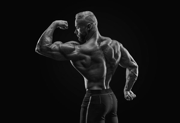 Silhouette of a strong bodybuilder. View from the back. Confident young fitness athlete with a powerful body and perfect abs. Black and white photography. Dramatic light