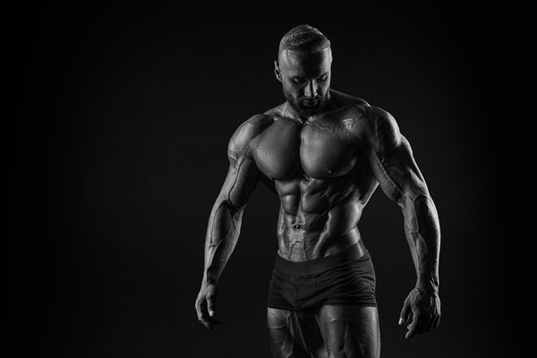 Silhouette of a strong bodybuilder. Confident young fitness athlete with a powerful body and perfect abs. Black and white photography. Dramatic light. Mixed media