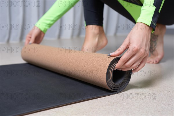 Image of a young woman in a gymnastics suit rolling up a mat after a workout. The concept of fitness