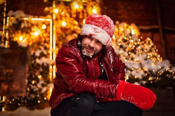 Man dressed as Santa Claus poses on a street decorated with garlands. New Year and Christmas concept. Mixed media