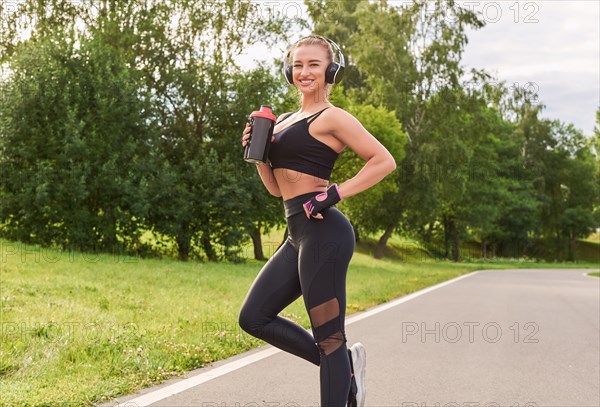 Girl posing with a sports nutrition shaker in the park. The concept of a healthy lifestyle. Sports Equipment. Fitness style advertisement. Mixed media