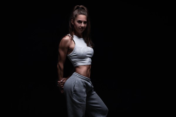 Athletic fitness woman posing in the studio on a dark background. Photo of an attractive woman in fashionable sportswear. Sports and healthy lifestyle. Mixed media