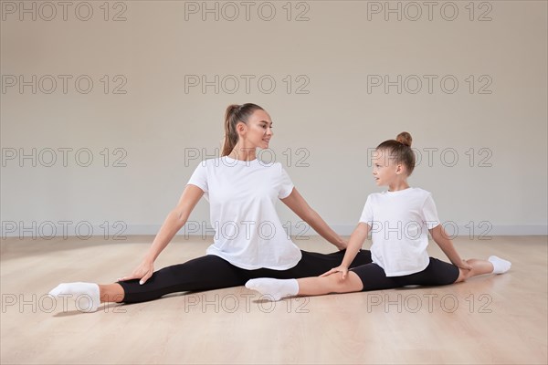 Beautiful female teacher and a little girl are sitting in the splits in a gymnastics class. The concept of education