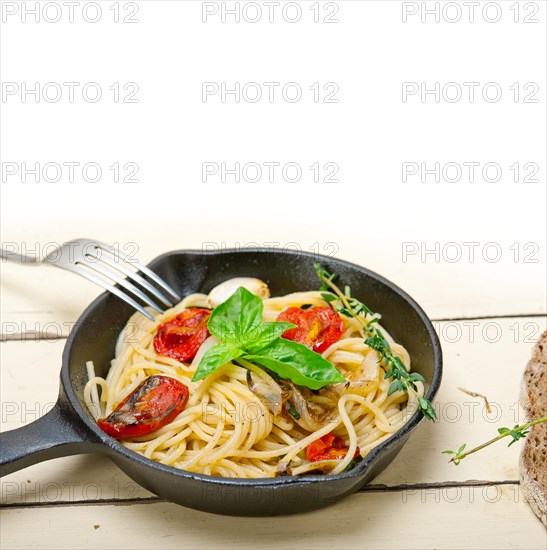 Italian spaghetti pasta with baked tomatoes basil and thyme sauce on a cast iron skillet