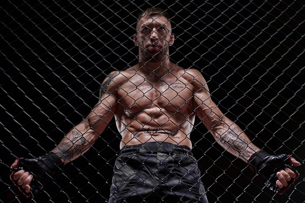 Portrait of a powerful fighter behind the steel bars of the octagon. The concept of sports