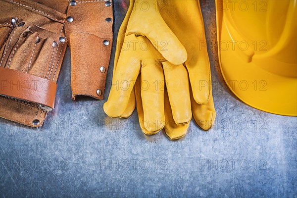 Yellow leather safety gloves tool belt hard hat on metallic background construction concept