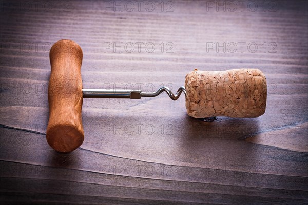 Corkscrew twisted in corks of champagne on vinatge wooden board close up alcohol concept