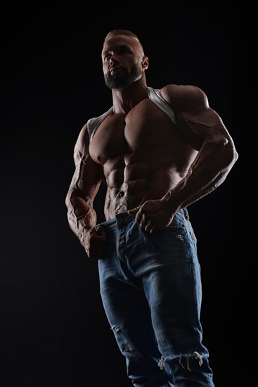 Muscular model man in white t-shirt on a black background. Sporty guy showing his big shoulders