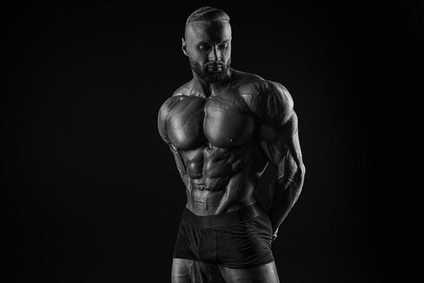 Silhouette of a strong bodybuilder. Confident young fitness athlete with a powerful body and perfect abs. Black and white photography. Dramatic light. Mixed media