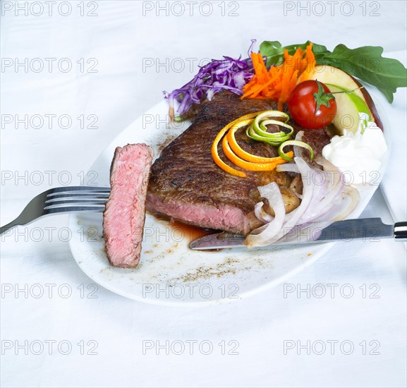 Fresh juicy beef ribeye steak grilled with lemon and orange peel on top and vegetables beside with sour cream