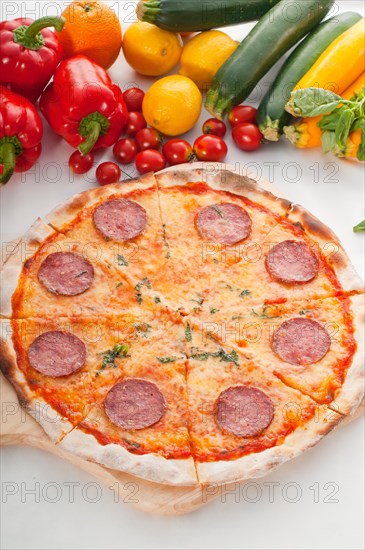 Italian original thin crust pepperoni pizza with fresh vegetables on background