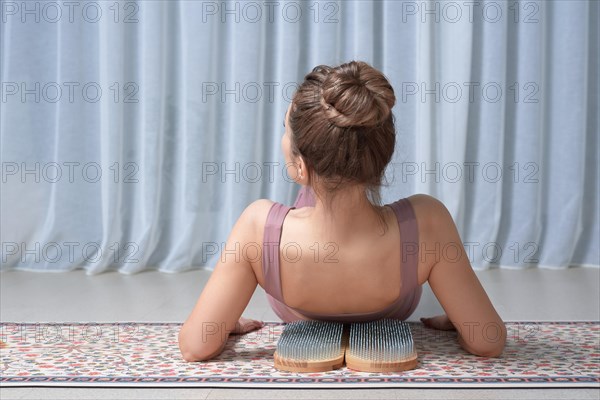 Image of a young woman in a gymnastic suit lying on a sadhu board on a mat in a bright studio. The concept of fitness