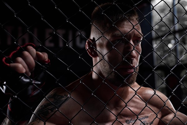 Dramatic image of a mixed martial arts fighter standing in an octagon cage. The concept of sports