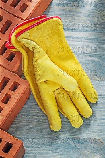 Red bricks leather protective gloves on wooden board top view building concept