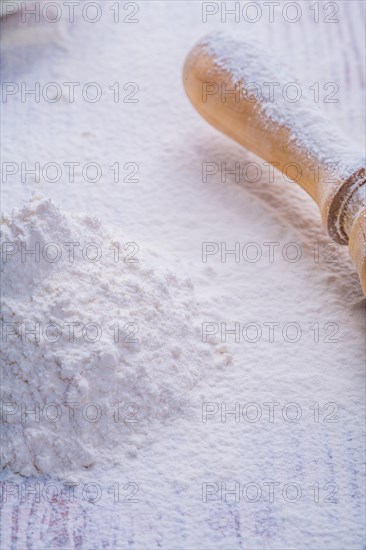 Small pile of white natural flour and wooden rolling pin in vertical version