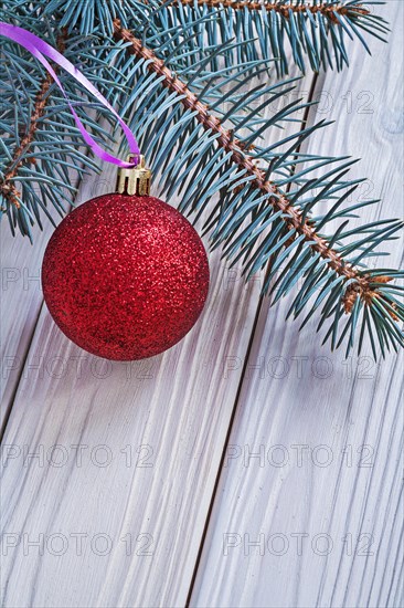 Matt red Christmas bauble and fir tree branch on a white wooden board