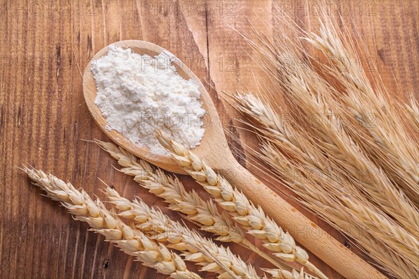 Flour in wooden spoon and wheat ears on vintage board food and drink concept