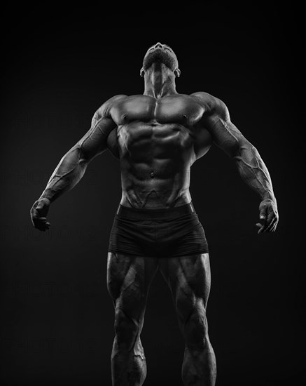 Silhouette of a strong bodybuilder. Confident young fitness athlete with a powerful body and perfect abs. Black and white photography. Dramatic light. Mixed media