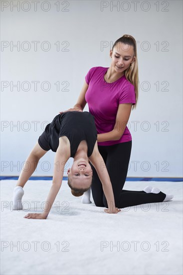 Training in the gym class. A little girl under the guidance of a trainer performs exercises. Gymnastics concept. Mixed media