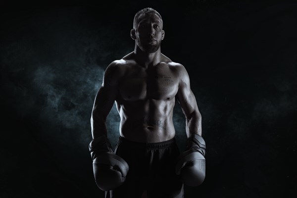 Kickboxer in black gloves posing on a background of smoke. The concept of mixed martial arts. MMA