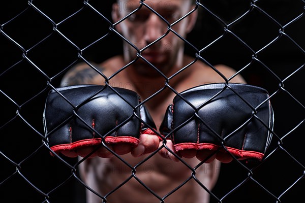 Dramatic image of a mixed martial arts fighter standing in an octagon cage. The concept of sports