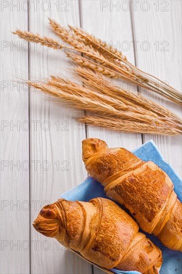 Croissants and ears of wheat on white wooden boards
