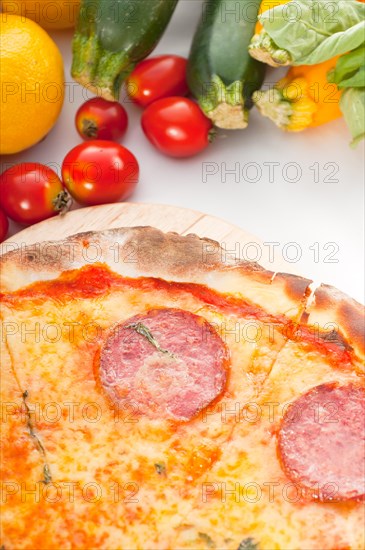 Italian original thin crust pepperoni pizza with fresh vegetables on background