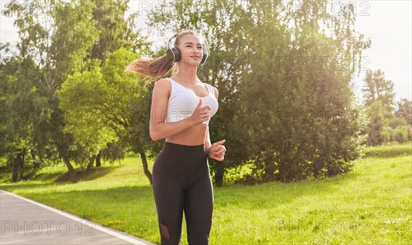 Fitness girl in sportswear runs through the evening sunny park. Healthy lifestyle. Mixed media