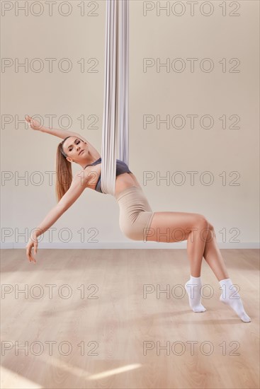 Image of a beautiful woman posing in a bright studio near the hammocks. The concept of airstretching. Fitness and sports