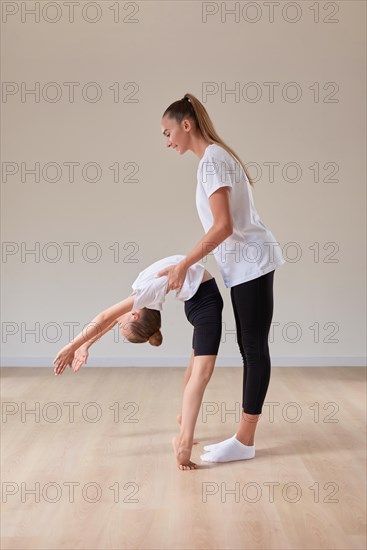 Beautiful female teacher helps a little girl stretch in a gymnastics class. The concept of education