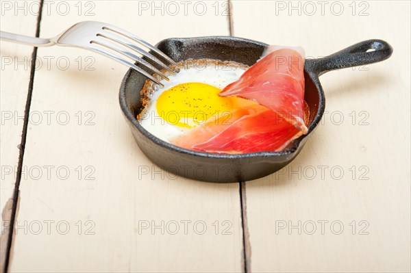 Fried egg sunny side up with Italian tyrolean speck smoked ham on a skillet