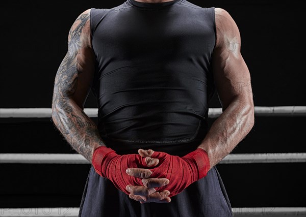 Red bandages on the hands of a kickboxer against the background of the ropes of the ring. The concept of mixed martial arts. MMA