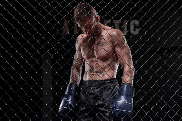 Dramatic image of a mixed martial arts fighter standing in an octagon cage. The concept of sports