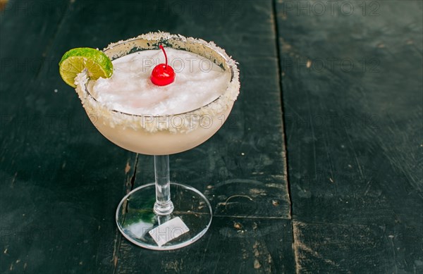 Frozen coconut margarita with lemon slice served on wooden table. Close up of delicious frozen coconut cocktail with cherry