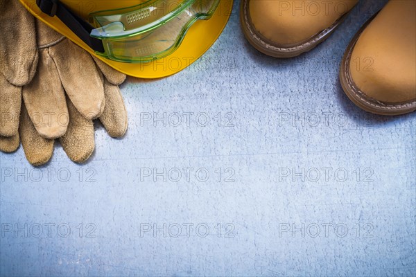 Composition of safety waterproof boots leather gloves building helmet and working glasses on scratched metallic background construction concept