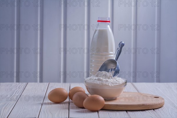 Horizontal view eggs flour in bowl scoop bottle milk on white lacquered old wooden board food and drink concept
