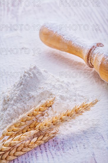 Wheat ears on a pile of white flour and a wooden rolling pin
