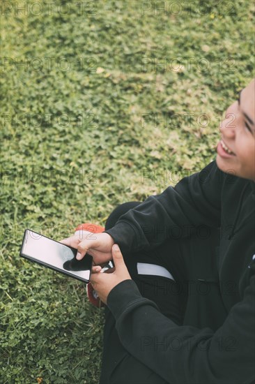 Cheerful teenager of Latino descent smiles as he looks at his smartphone screen. The boy's relaxed posture and cheerful expression convey a sense of contentment. Background blurred to focus attention on the boy and his phone