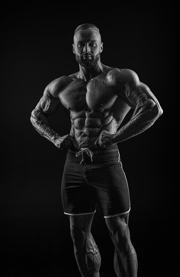 Silhouette of a strong bodybuilder. Confident young fitness athlete with a powerful body and perfect abs. Black and white photography. Dramatic light. Mixed media