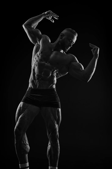 Silhouette of a strong bodybuilder. Confident young fitness athlete with a powerful body and perfect abs. Black and white photography. Dramatic light. Mixed media