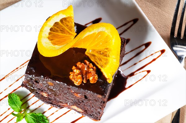 Fresh baked delicious chocolate and walnuts cake with slice of orance on top and mint leaf