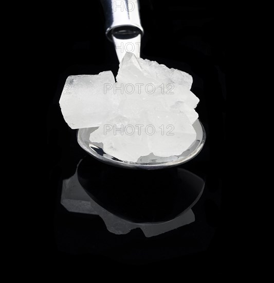 Crystal sugar on a spoon over black reflective surface background