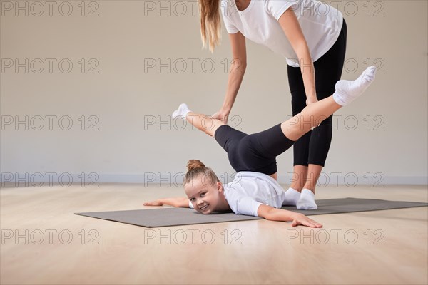 Beautiful female teacher helps a little girl stretch in a gymnastics class. The concept of education