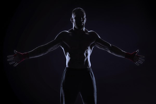 Kickboxer in red bandages poses on a blue background with his arms apart. The concept of mixed martial arts. MMA