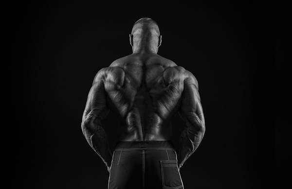 Silhouette of a strong bodybuilder. View from the back. Confident young fitness athlete with a powerful body and perfect abs. Black and white photography. Dramatic light