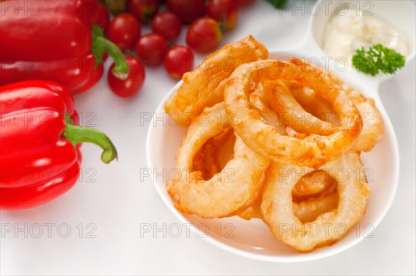 Golden deep fried onion rings served with mayonnaise dip and fresh vegetables oln background