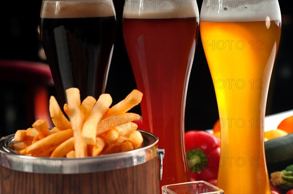 Fresh french fries on a wood bucket with selection of beers and fresh vegetables on background