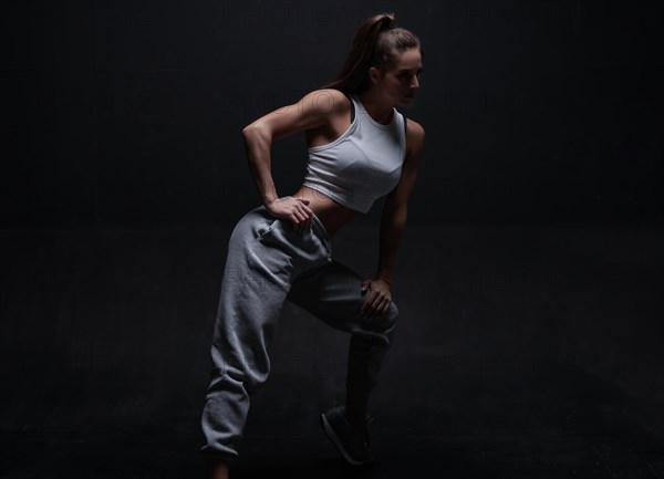 Athletic fitness woman posing in the studio on a dark background. Photo of an attractive woman in fashionable sportswear. Sports and healthy lifestyle. Mixed media