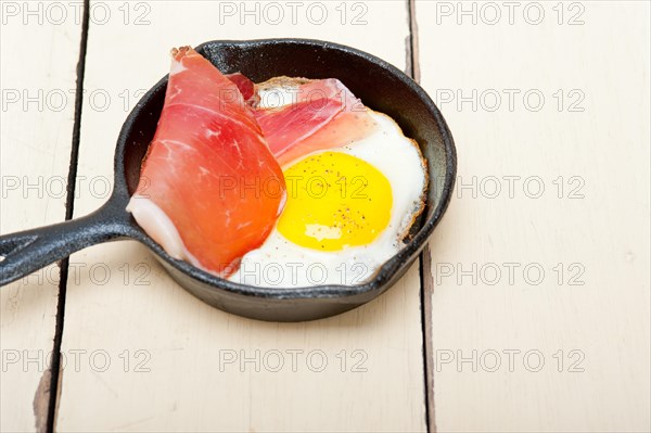 Fried egg sunny side up with Italian tyrolean speck smoked ham on a skillet